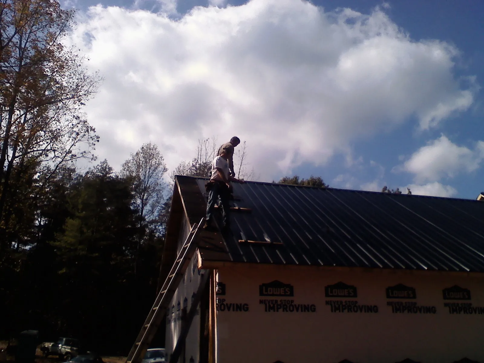 Roofer fastening dark metal panels high against a cloudy sky, from a Roof Inspection job in Grovertown