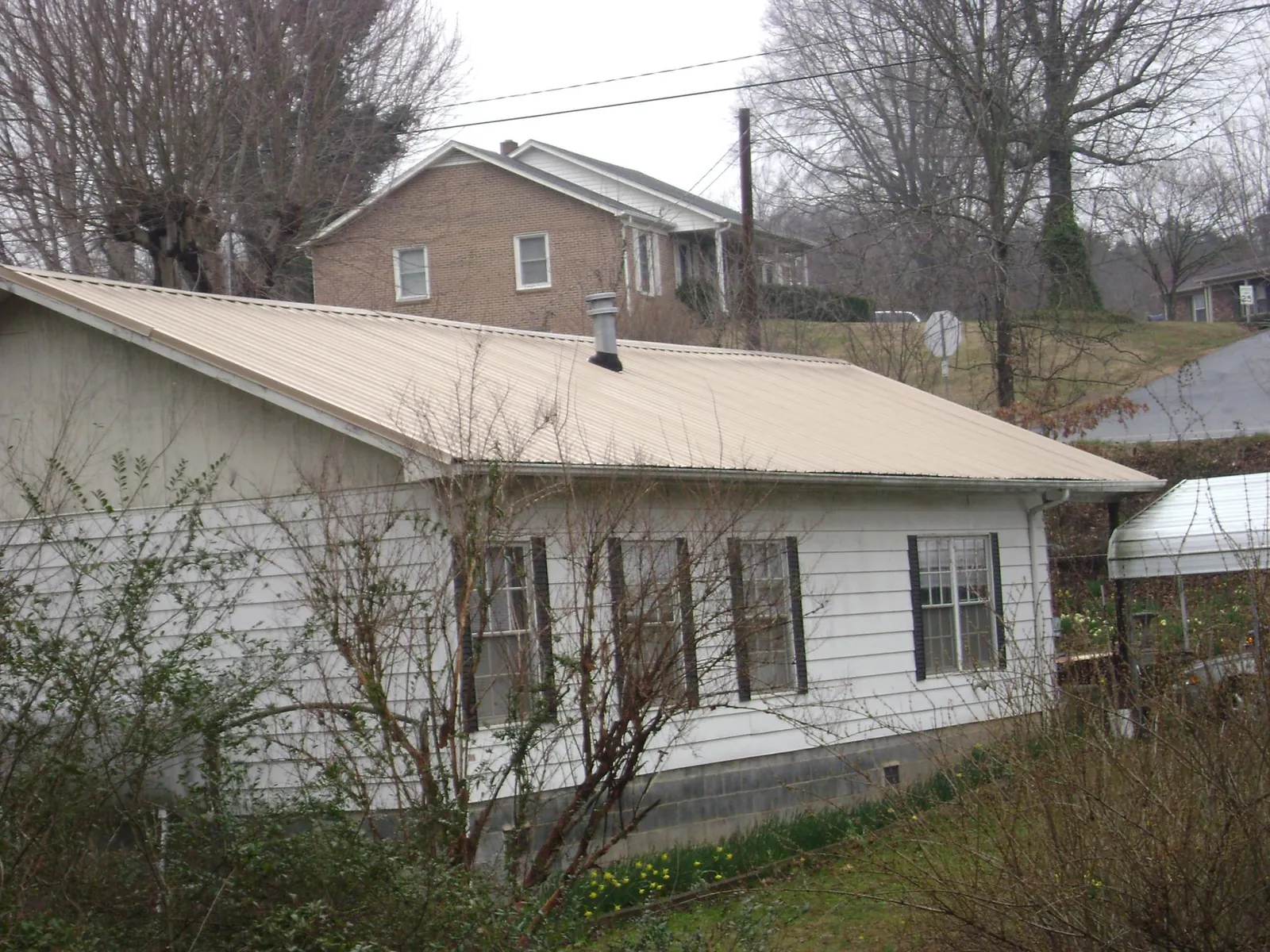 Tan metal roof on a white sided house set into a hillside — Commercial Roofing by Roofing Brothers in Grovertown